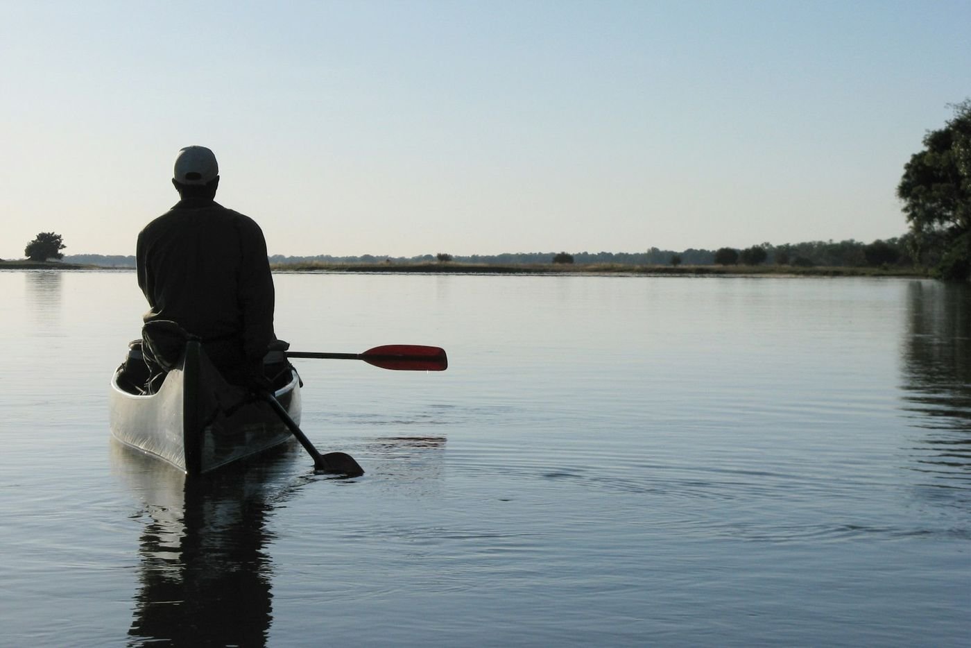 A paddler in a canoe on calm water at dawn