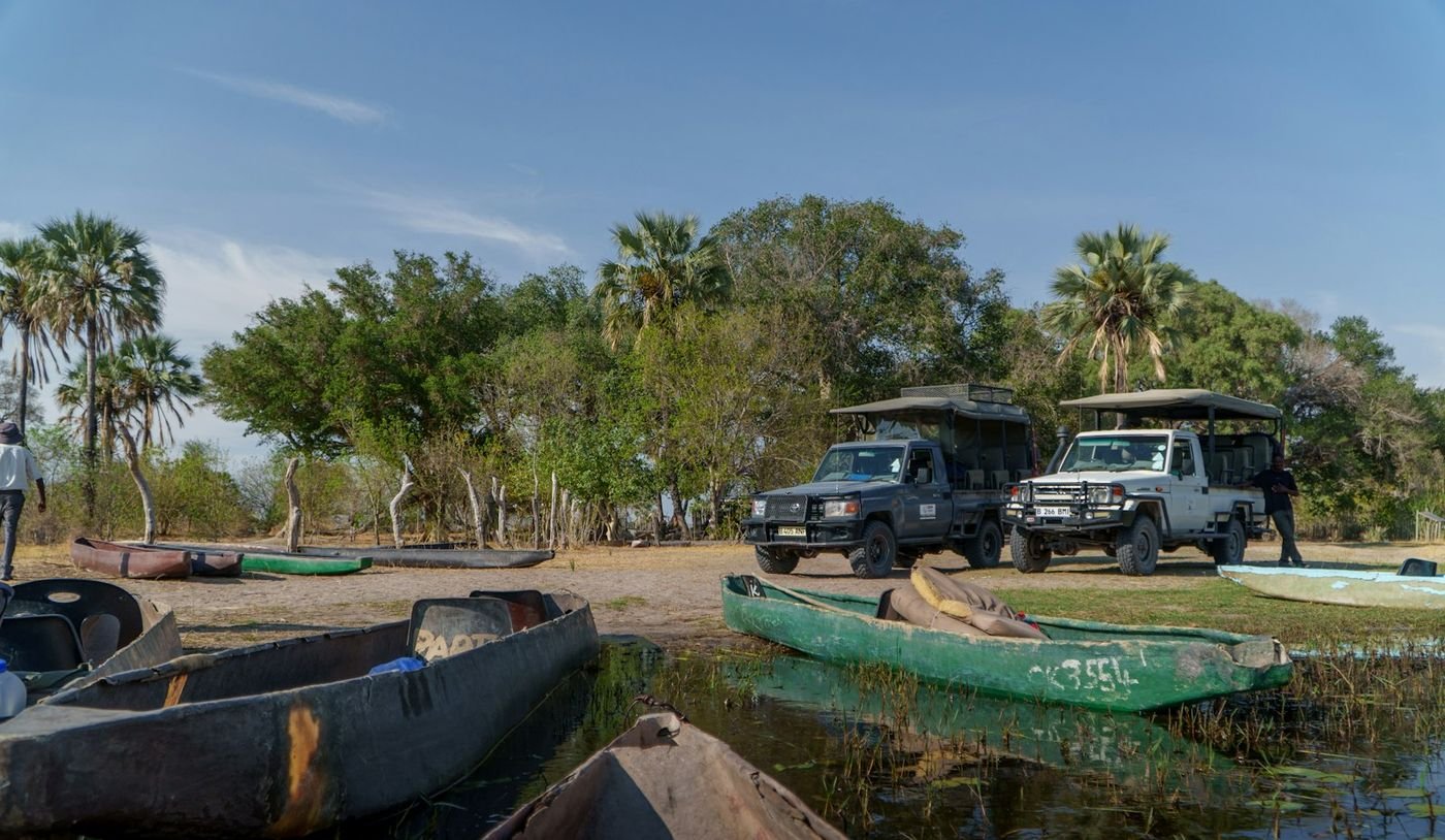 Open safari vehicles parked by the water in the bush