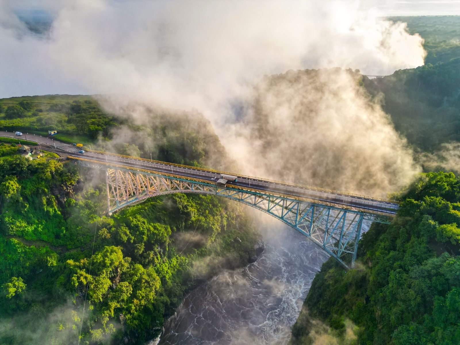 Aerial view of the Victoria Falls Bridge over the Batoka Gorge, with spray rising from the Falls